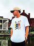 Person wearing a white t-shirt with a graphic design, standing by a waterfront with buildings in the background.